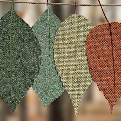 Tweed leaves hung on a clothesline against forest backdrop. Leaves are mostly shades of green but also burnt orange to symbolize this post goes beyond classic fall books for kids to also cover fall kids' books for warmer climates.