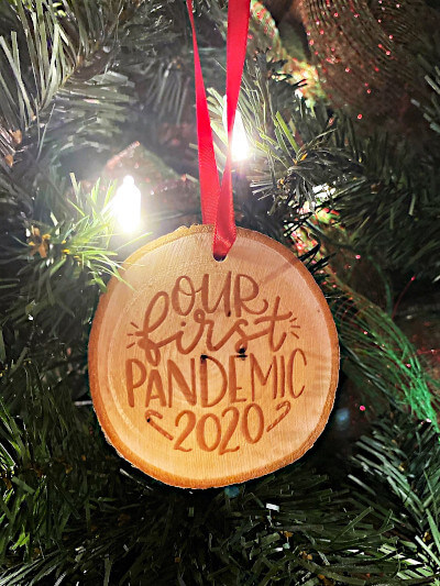 Wooden ornament saying "our first pandemic 2020" hangs on a Christmas tree as a reminder of all we have made it through this year