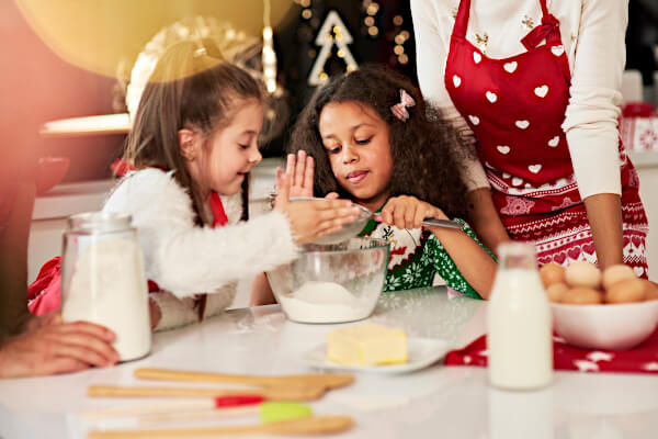 Two girls have fun with a Christmas baking activity while mom looks on; baking a Christmas morning pastry can be a fun way to celebrate Jesus.
