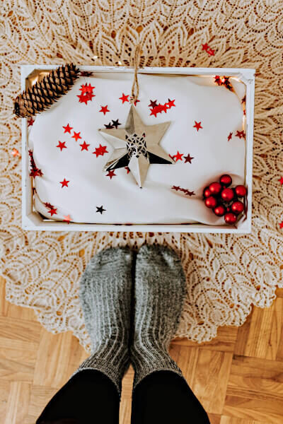 giving ornaments is a way to celebrate family moments; image: shiny ornament in a box with red confetti next to a person's sock feet