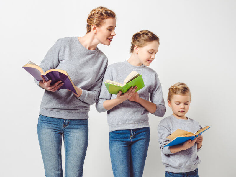a young boy is reading a book with his mom and sister, each holding their own books open and looking at his