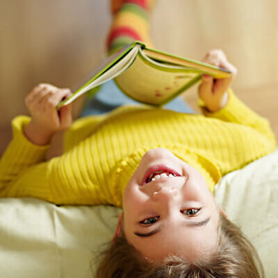 child taking a break from reading a book to look up at the camera with a big smile