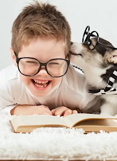 Gratitude Books for Kids - Little boy with glasses trying to read a book while a cute dog with glasses licks his face