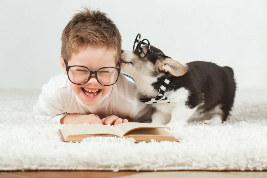 Gratitude Books for Kids - Little boy with glasses trying to read a book while a cute dog with glasses licks his face
