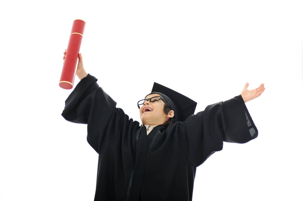 a young child with arms up celebrating graduation in a cap and gown for this milestone moment